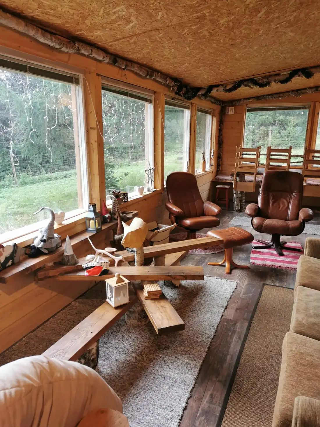 Véranda lumineuse du chalet, fauteuils en cuir et grandes fenêtres sur la forêt