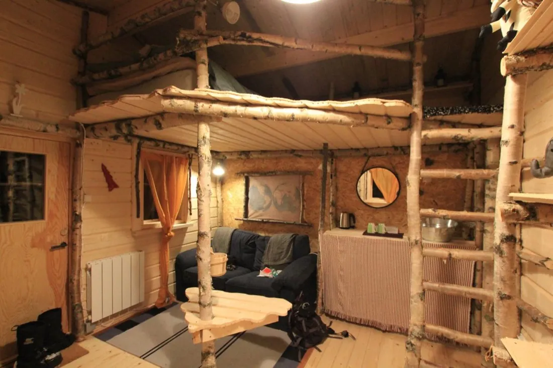 Intérieur du chalet en madrier : mezzanine et structures en bouleau brut, coin salon et petite cuisine