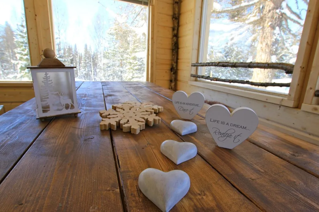 Grande table en bois brut du chalet, décor de flocons et de cœurs, fenêtres ouvertes sur la forêt enneigée