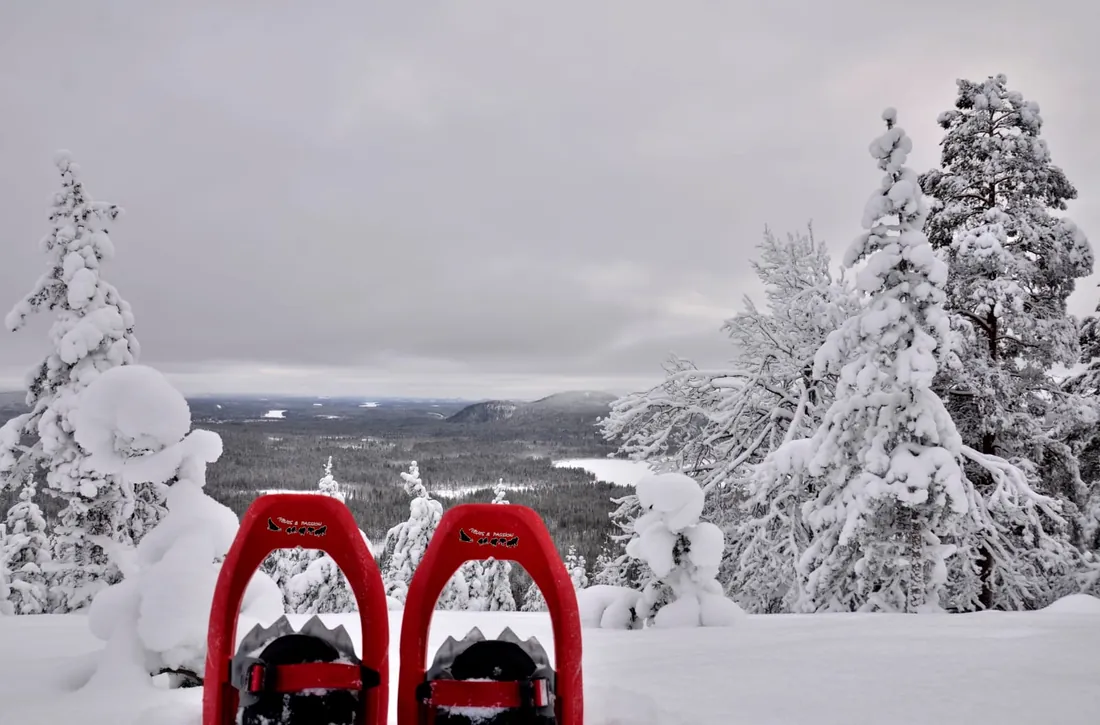 Raquettes rouges face à un vaste panorama de forêt givrée et de lacs gelés en Laponie