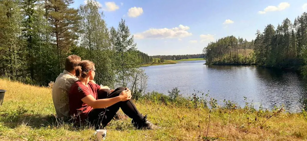 Couple enlacé au bord d'un lac forestier ensoleillé, herbe dorée et ciel bleu d'été