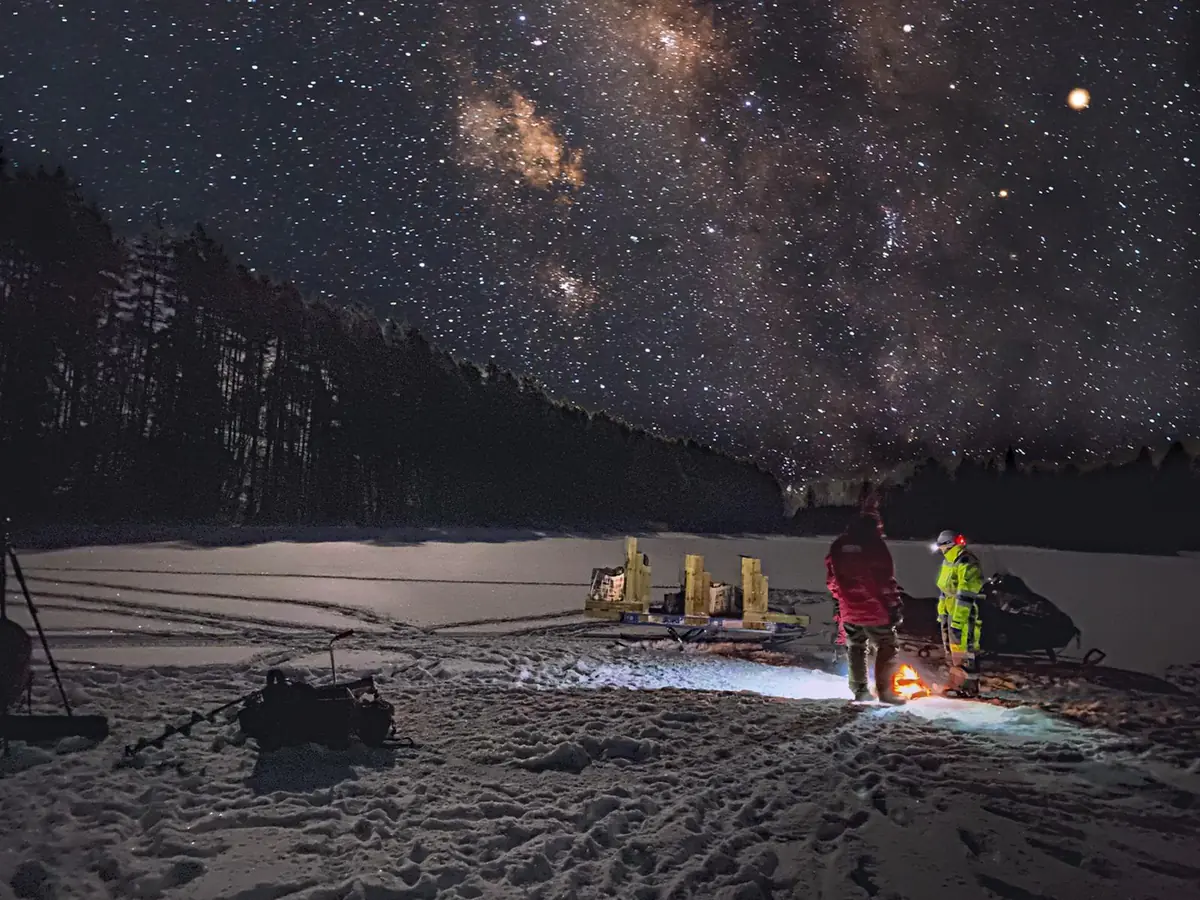 Voie lactée étoilée au-dessus de motoneiges et d'un feu sur un lac gelé la nuit