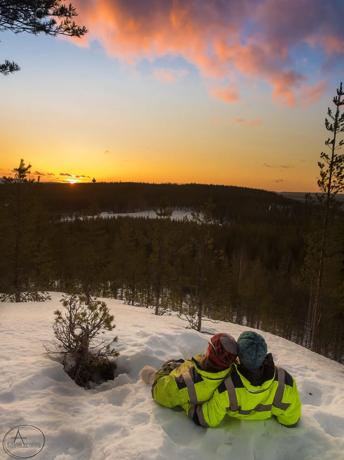 Aurélie et Rémy enlacés, contemplant un coucher de soleil sur la forêt enneigée