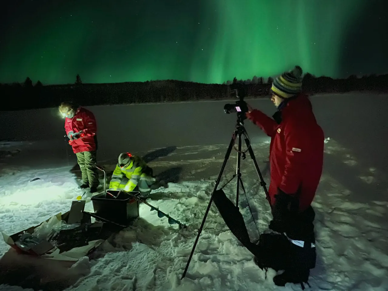 Visiteurs en parkas rouges photographiant une aurore boréale verte sur un lac gelé la nuit